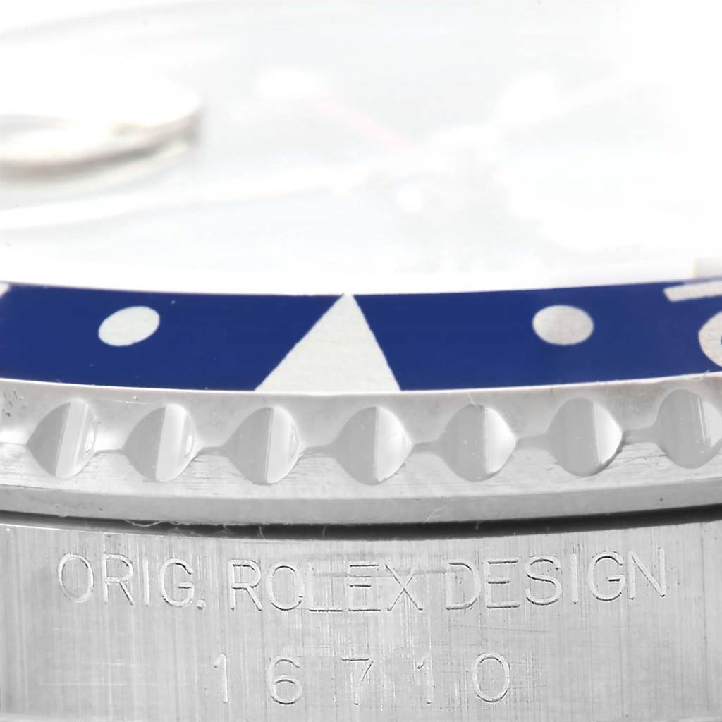 This close-up of a Rolex GMT-Master 16710 Men's Stainless Steel Black Dial 16710 Men's Stainless Steel Black Dial watch shows the edge of the bezel and engraved text on the case.