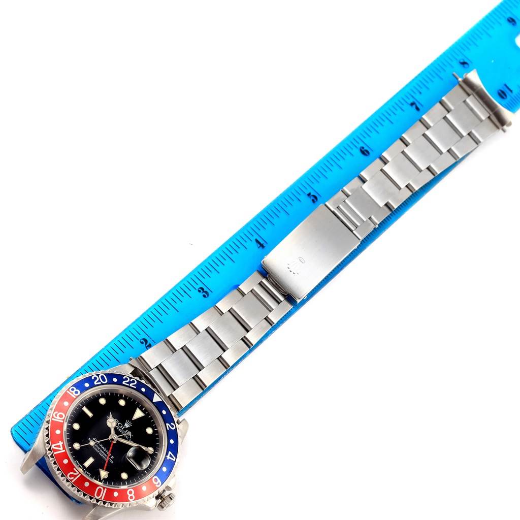 The image shows a Rolex GMT-Master 16710 Men's Stainless Steel Black Dial 16710 Men's Stainless Steel Black Dial watch laid flat next to a ruler, displaying the watch case, bezel, and bracelet.