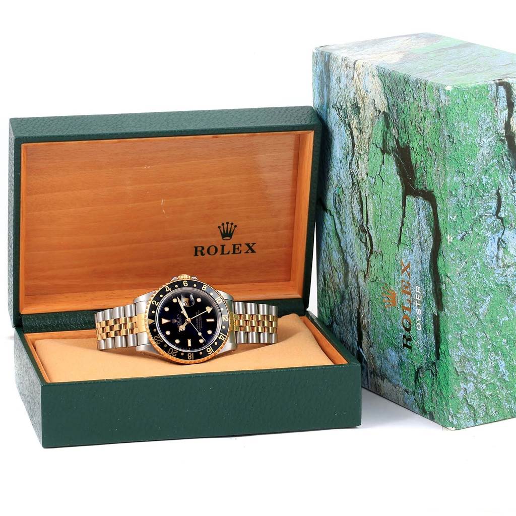 The Rolex GMT-Master 16713 Men's Stainless Steel Black Dial 16713 Men's Stainless Steel Black Dial watch is displayed front-facing inside an open green and wood box, with its outer box beside it.