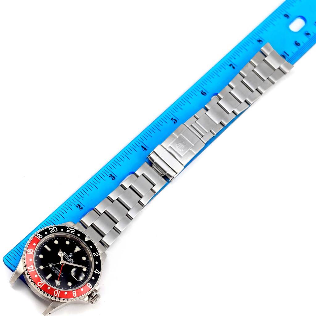 The Rolex GMT-Master 16710 Men's Stainless Steel Black Dial 16710 Men's Stainless Steel Black Dial watch is shown from a top-down angle, displaying its face, bezel, and metal bracelet alongside a blue ruler.