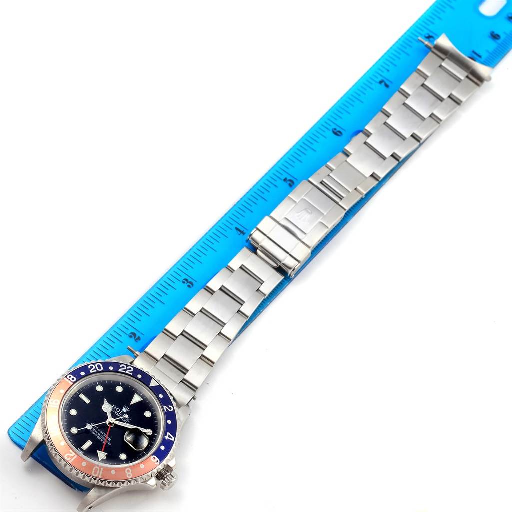 The image shows a Rolex GMT-Master 16700 Men's Stainless Steel Black Dial 16700 Men's Stainless Steel Black Dial watch lying flat next to a blue ruler, displaying its face, bezel, and metal bracelet.