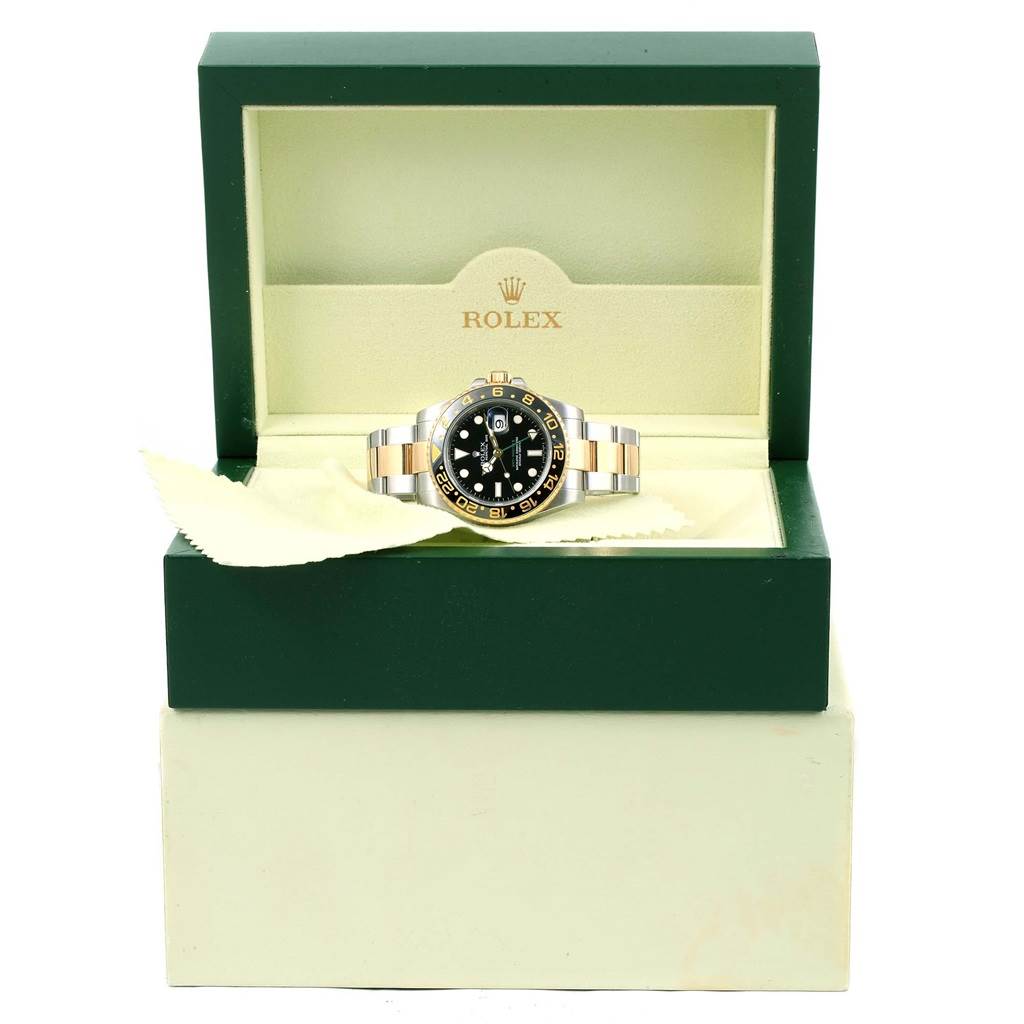 The Rolex GMT-Master 116713 Men
s Stainless Steel Black Dial 116713 Men
s Stainless Steel Black Dial watch is displayed front-facing, inside an open green and cream Rolex box with a cloth nearby.