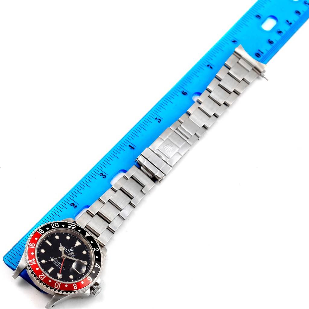 The image shows a Rolex GMT-Master 16710 Men's Stainless Steel Black Dial 16710 Men's Stainless Steel Black Dial watch laid flat with the dial, bezel, and metal bracelet visible alongside a blue ruler.