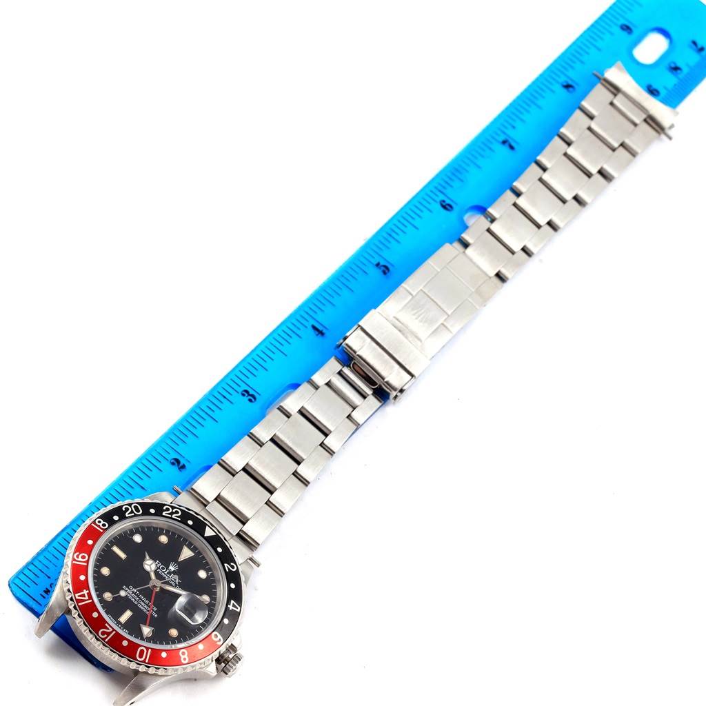 The image shows a Rolex GMT-Master 16700 Men's Stainless Steel Black Dial 16700 Men's Stainless Steel Black Dial watch laid out flat alongside a blue ruler, displaying the entire watch and bracelet.