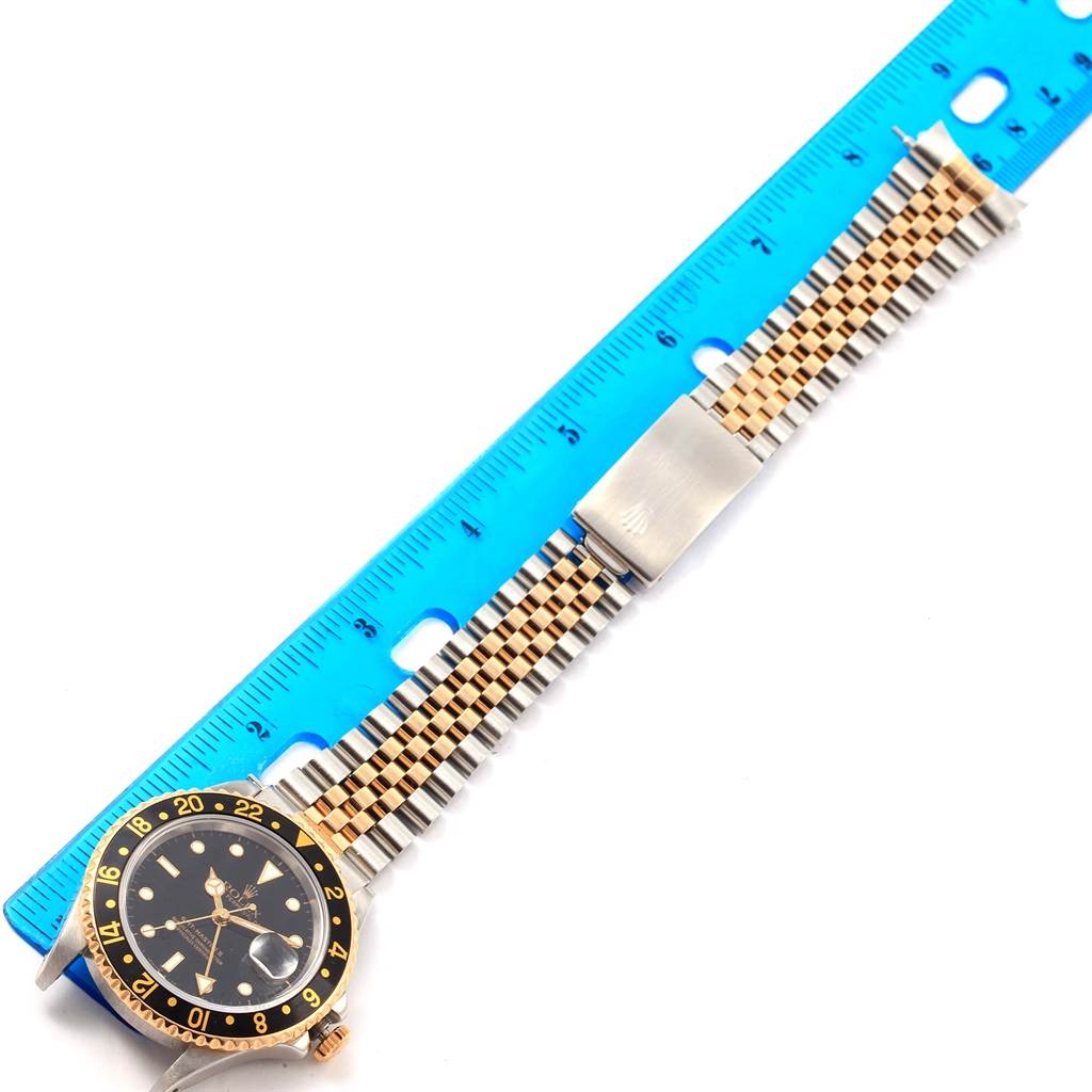 This image shows a Rolex GMT-Master 16713 Men's Stainless Steel Black Dial 16713 Men's Stainless Steel Black Dial watch laid flat with a mix of gold and silver bracelet links and a blue measuring ruler beside it.