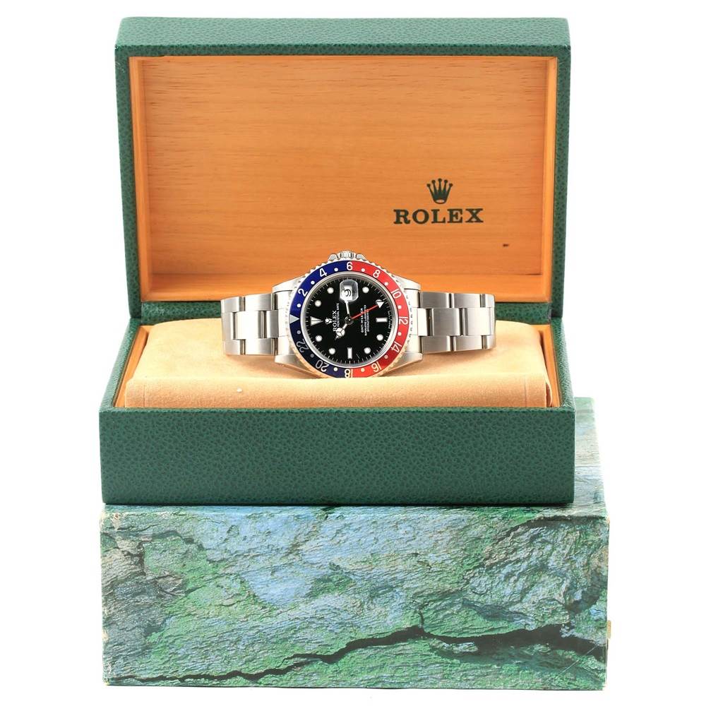 A Rolex GMT-Master 16700 Men
s Stainless Steel Black Dial 16700 Men
s Stainless Steel Black Dial watch is shown in its box, displaying the face, bezel, and metal bracelet from a front angle.