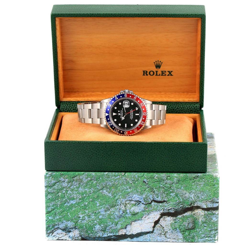 The Rolex GMT-Master 16710 Men's Stainless Steel Black Dial 16710 Men's Stainless Steel Black Dial watch is shown front-facing, displayed in an open green and wood box.
