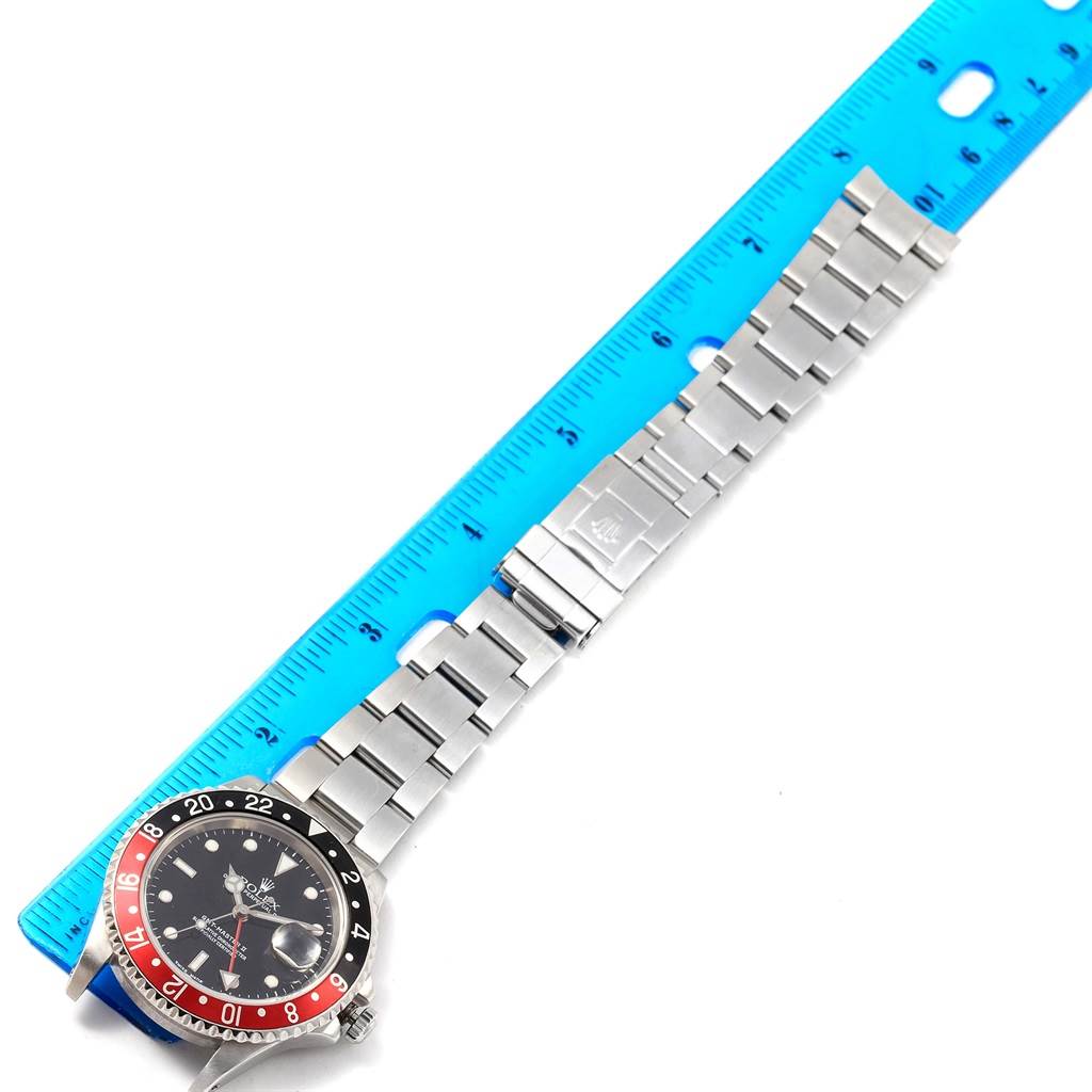 The image shows the front of a Rolex GMT-Master 16710 Men's Stainless Steel Black Dial 16710 Men's Stainless Steel Black Dial watch with its bracelet beside a blue ruler for scale.