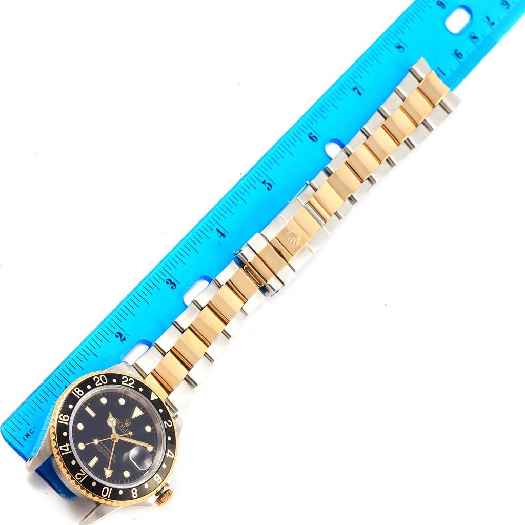 The image shows a Rolex GMT-Master 16713 Men's Stainless Steel Black Dial 16713 Men's Stainless Steel Black Dial watch laid flat with a metal and gold bracelet alongside a blue measuring ruler.