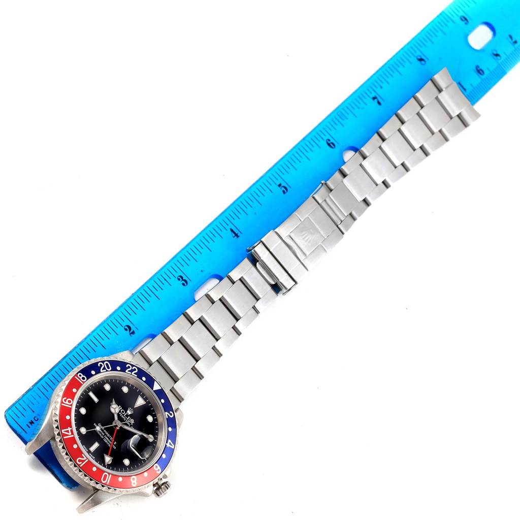 The image shows a Rolex GMT-Master 16710 Men
s Stainless Steel Black Dial 16710 Men
s Stainless Steel Black Dial watch with a "Pepsi" bezel and a steel bracelet laid out next to a blue ruler.