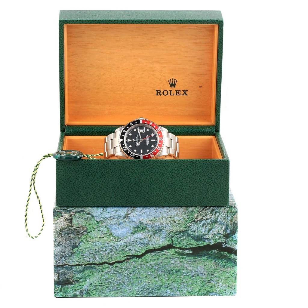 The Rolex GMT-Master 16710 Men's Stainless Steel Black Dial 16710 Men's Stainless Steel Black Dial watch is shown in an open green and beige box, viewed from the front.