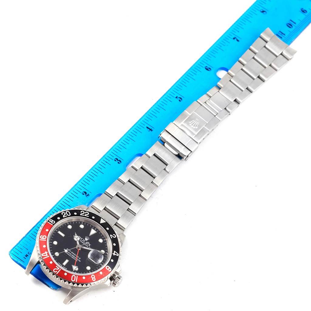 The Rolex GMT-Master 16710 Men's Stainless Steel Black Dial 16710 Men's Stainless Steel Black Dial watch is shown from a top-down angle, displaying its face, bezel, and metal bracelet next to a ruler.