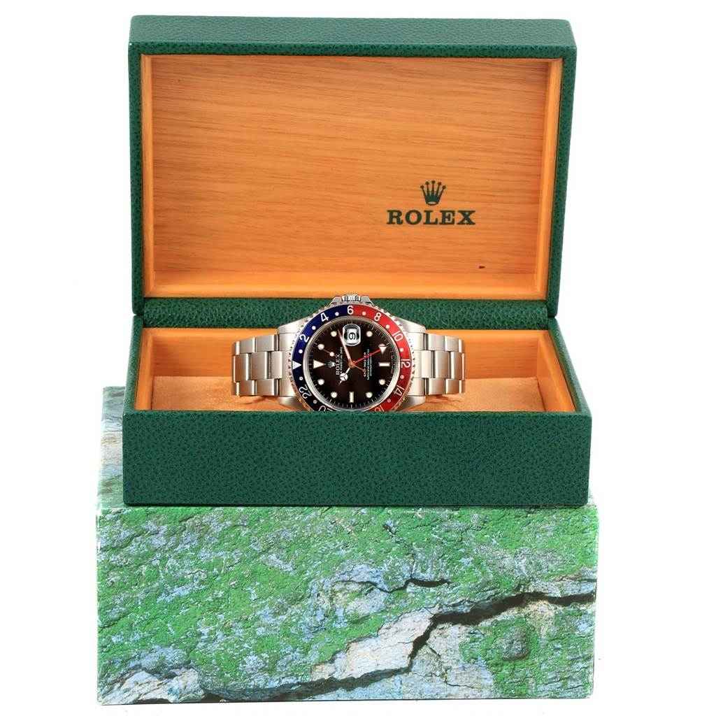 The Rolex GMT-Master 16700 Men's Stainless Steel Black Dial 16700 Men's Stainless Steel Black Dial watch is shown front-on inside its open green and wood-tone presentation box.