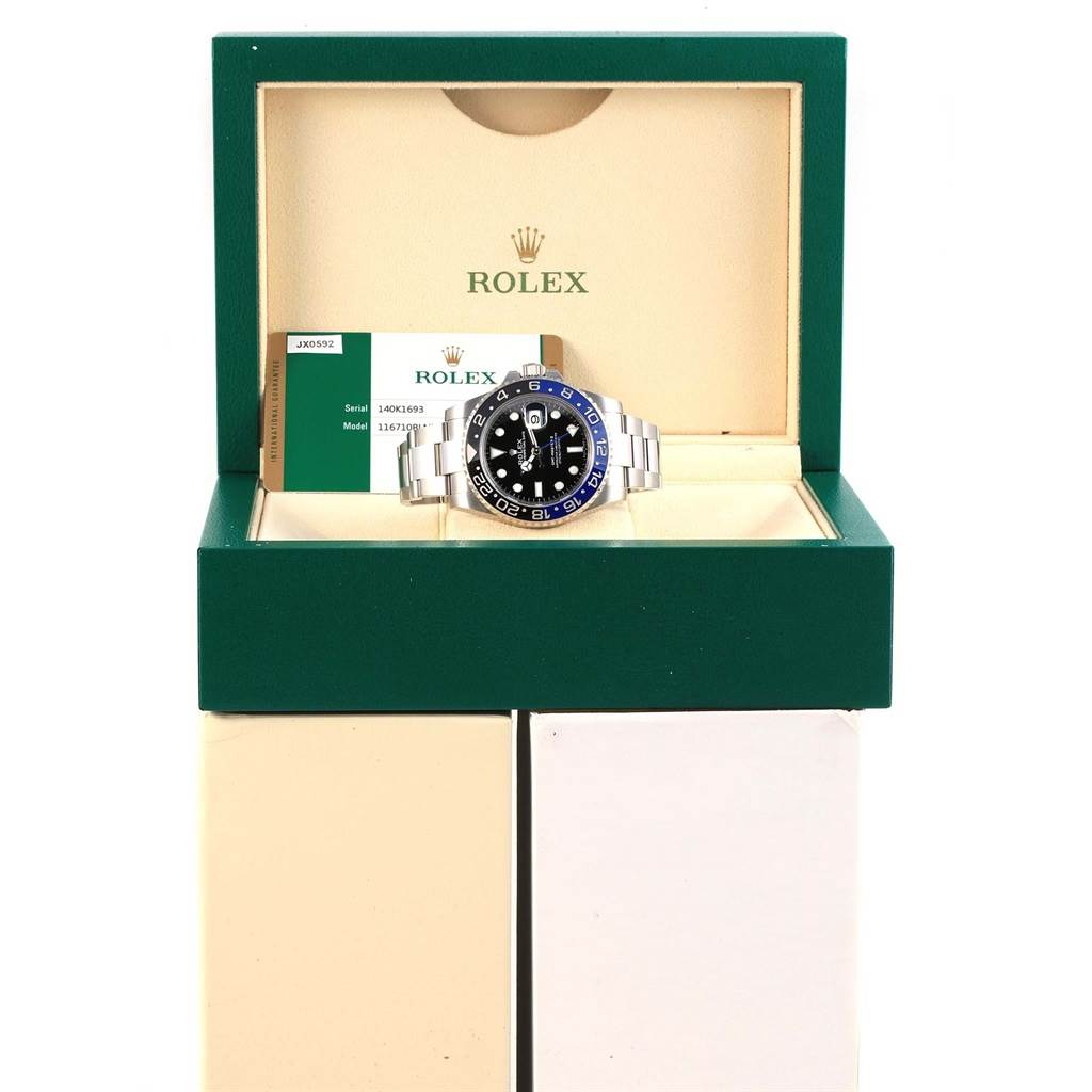 The image shows a Rolex GMT-Master 116710 Men
s Stainless Steel Black Dial 116710 Men
s Stainless Steel Black Dial watch with a black and blue bezel in its open box, along with paperwork.