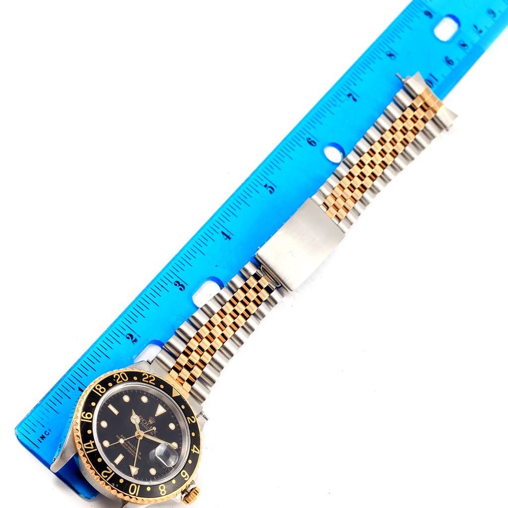 The image shows a Rolex GMT-Master 16713 Men's Stainless Steel Black Dial 16713 Men's Stainless Steel Black Dial watch laid flat next to a ruler, displaying its face, bezel, and bracelet.