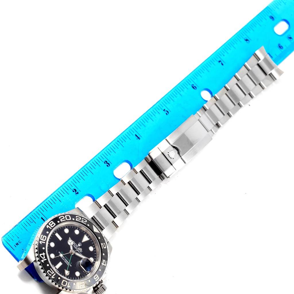 The image shows a top-down view of a Rolex GMT-Master 116710 Men's Stainless Steel Black Dial 116710 Men's Stainless Steel Black Dial watch with its bracelet aligned next to a blue ruler.