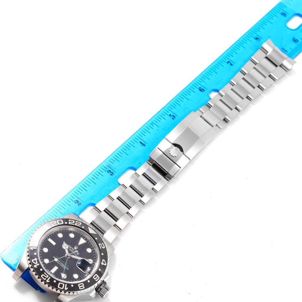 The Rolex GMT-Master 116710 Men's Stainless Steel Black Dial 116710 Men's Stainless Steel Black Dial watch is shown at a top-down angle, displaying its face, bezel, and stainless steel bracelet next to a ruler.