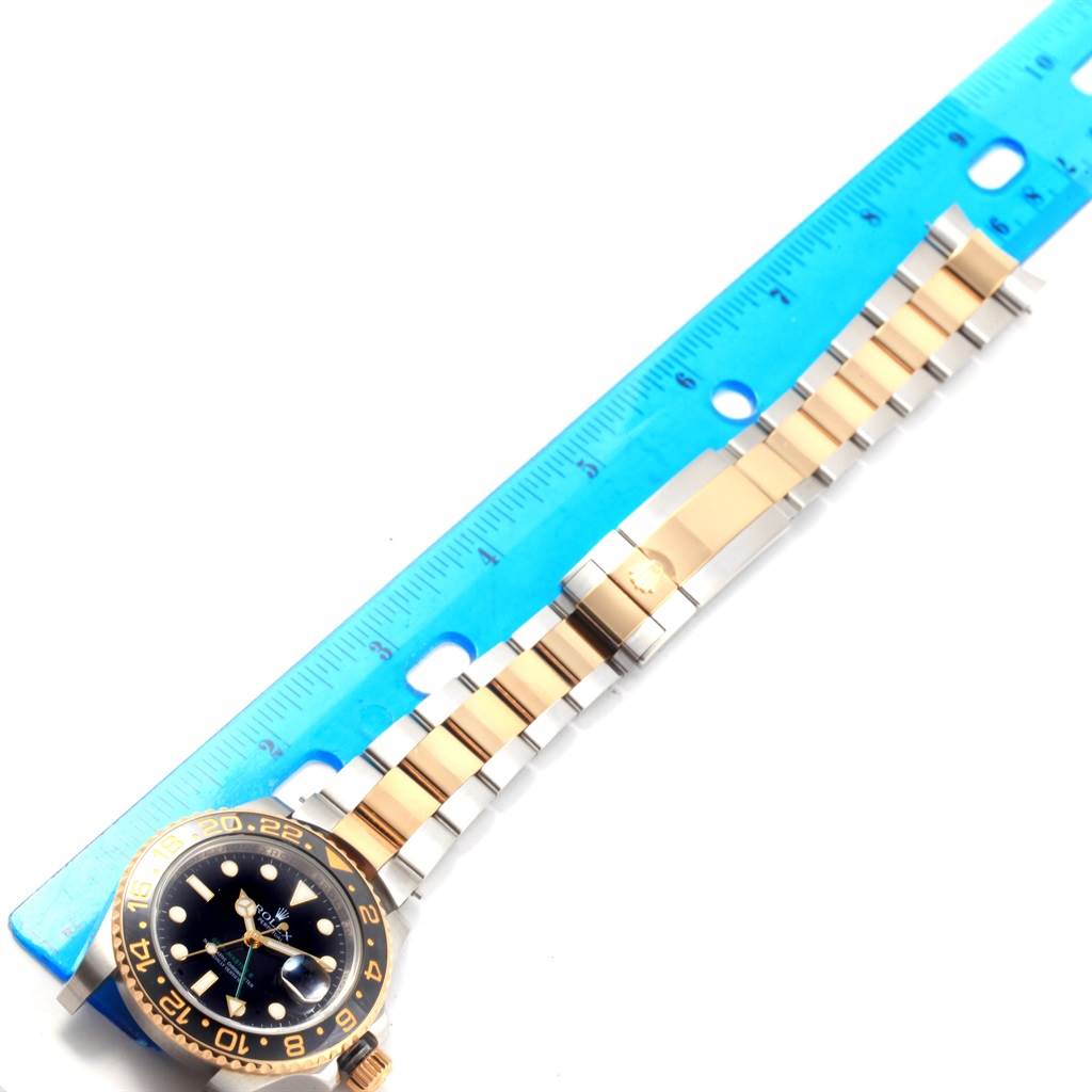 The image shows a side angle of a Rolex GMT-Master 116713 Men
s Stainless Steel Black Dial 116713 Men
s Stainless Steel Black Dial watch with its bracelet extended alongside a blue ruler for measurement.