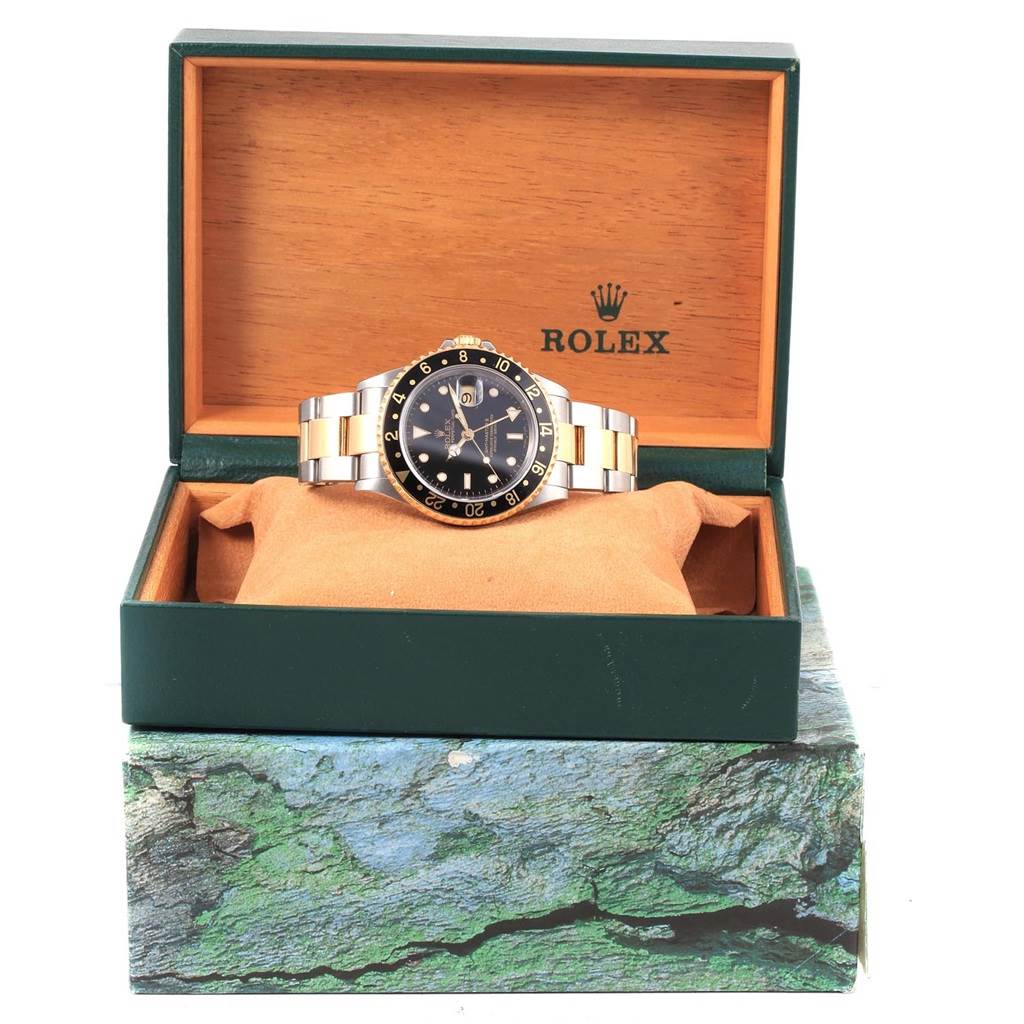 The Rolex GMT-Master 16713 Men's Stainless Steel Black Dial 16713 Men's Stainless Steel Black Dial watch is shown front-facing, displayed in its open green and wood box on a cushion.