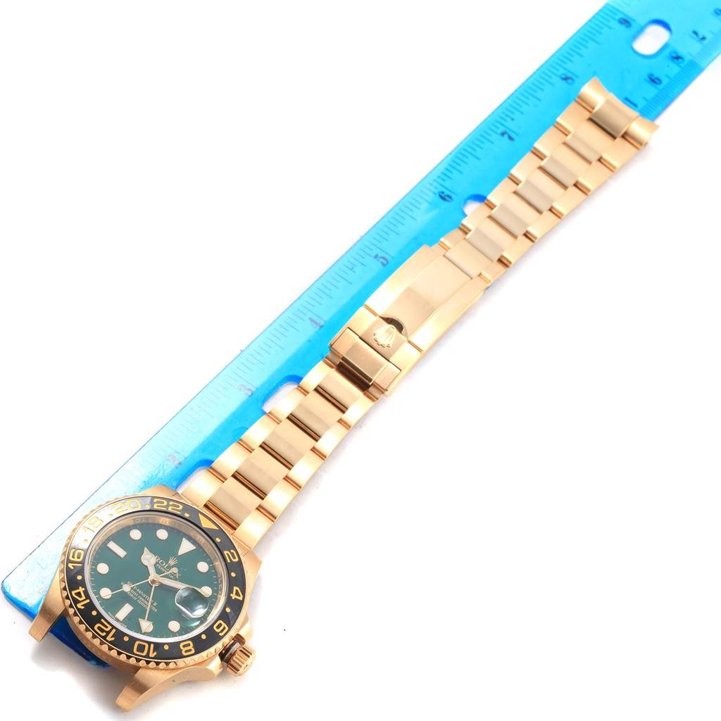 This image shows the Rolex GMT-Master 116718 Men's Yellow Gold Green Dial 116718 Men's Yellow Gold Green Dial watch from an angled top-down view, highlighting its face, bezel, and bracelet alongside a ruler for scale.