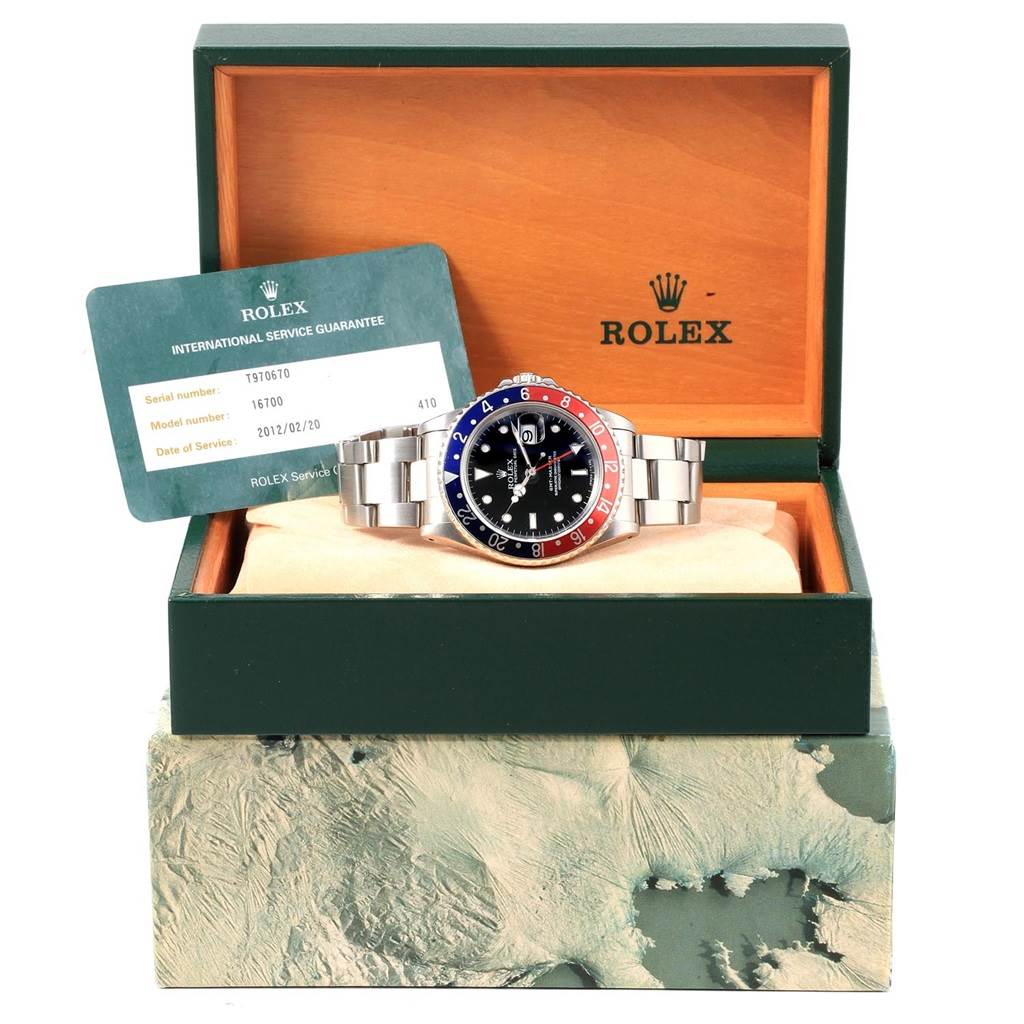 The Rolex GMT-Master 16700 Men's Stainless Steel Black Dial 16700 Men's Stainless Steel Black Dial watch is displayed front-facing in its open box with an International Service Guarantee card to the side.