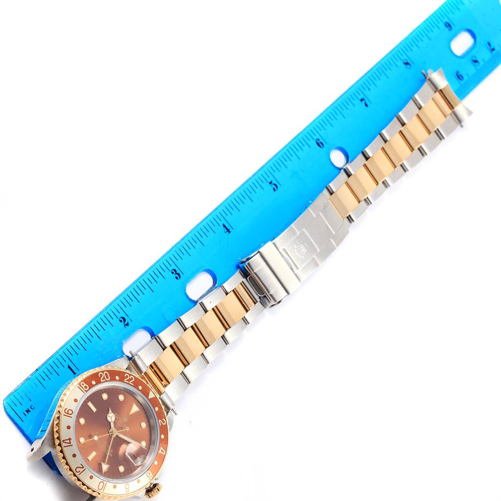 A Rolex GMT-Master 16713 Men's Stainless Steel Brown Dial 16713 Men's Stainless Steel Brown Dial watch laid flat with a two-tone bracelet shown next to a blue ruler for scale.