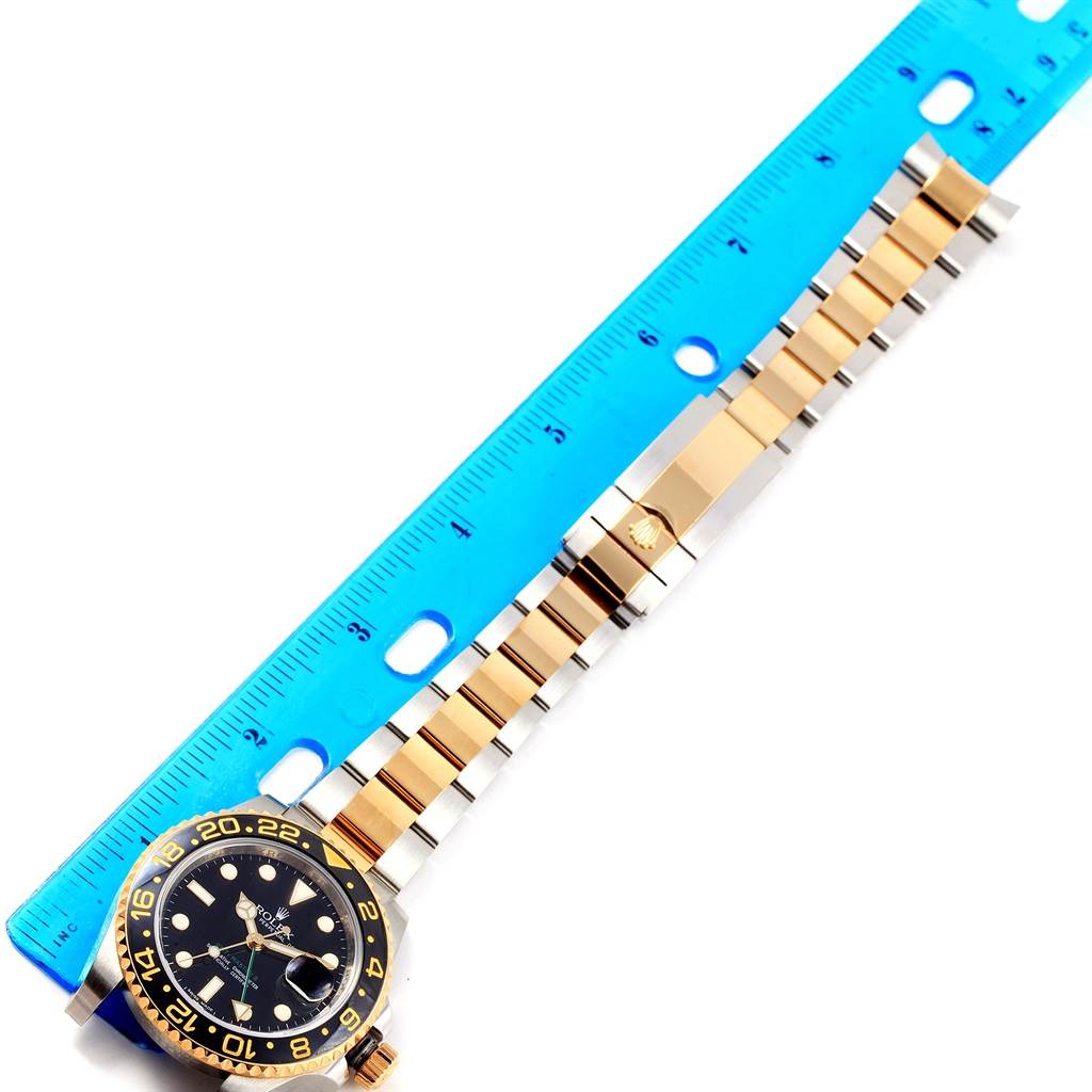 The Rolex GMT-Master 116713 Men
s Stainless Steel Black Dial 116713 Men
s Stainless Steel Black Dial watch is shown flat, displaying the face, bezel, and bracelet alongside a blue ruler for measurement.