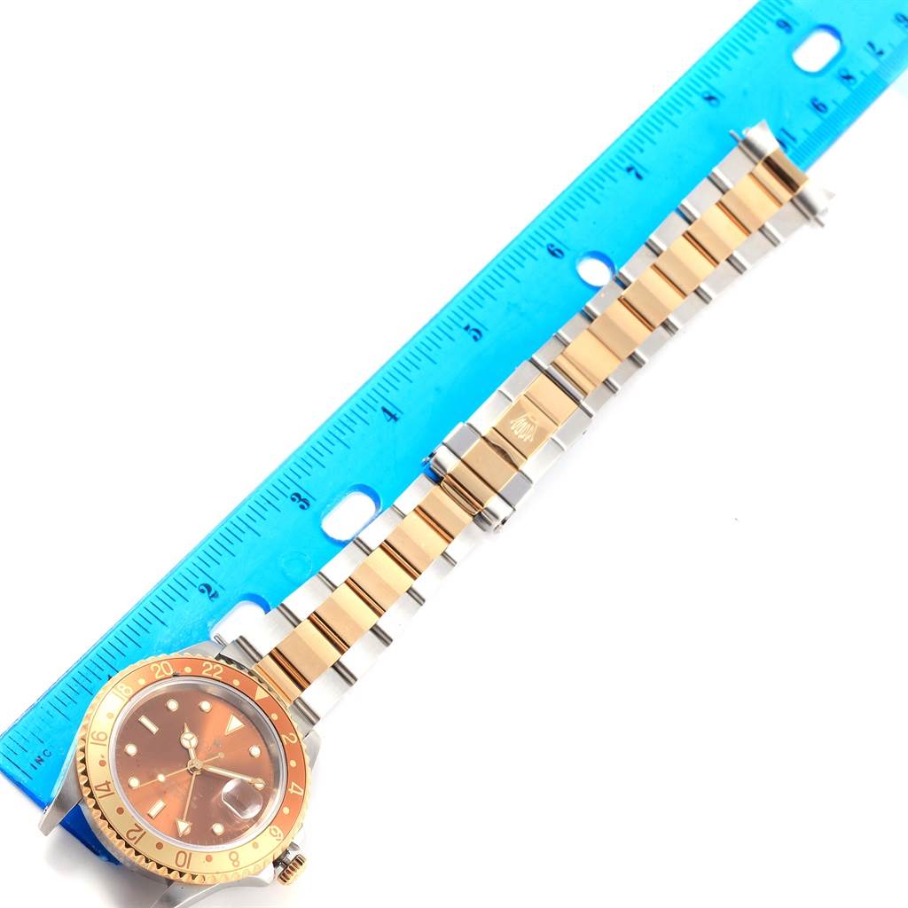 The image shows a top-down view of the Rolex GMT-Master 16713 Men's Stainless Steel Brown Dial 16713 Men's Stainless Steel Brown Dial, highlighting its two-tone bracelet and bezel alongside a blue ruler.