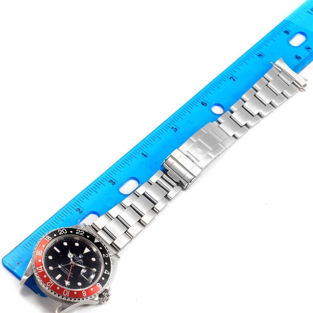 The image shows a Rolex GMT-Master 16700 Men's Stainless Steel Black Dial 16700 Men's Stainless Steel Black Dial watch laying flat next to a blue ruler, displaying its face, bezel, and metal bracelet.