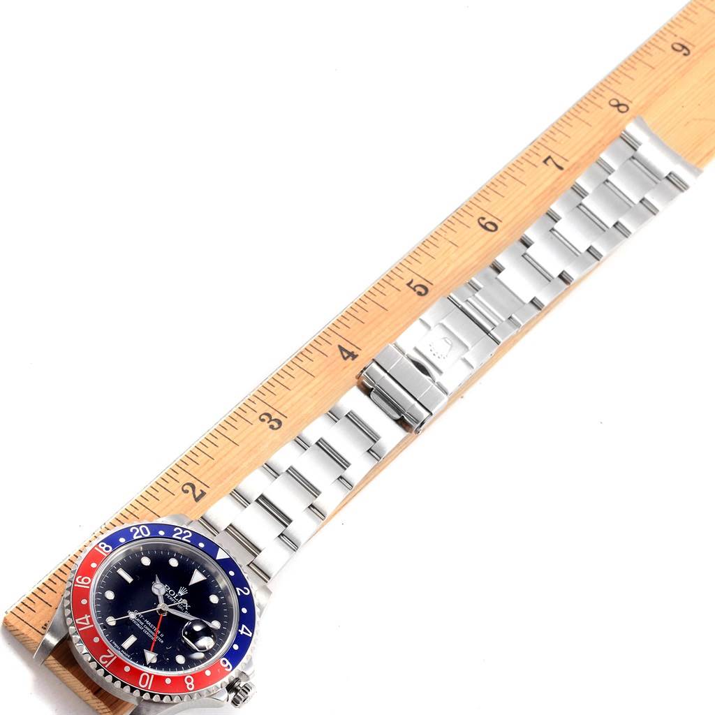 The image shows a top view of a GMT-Master Rolex watch next to a ruler for scale, highlighting the bezel, dial, and bracelet.