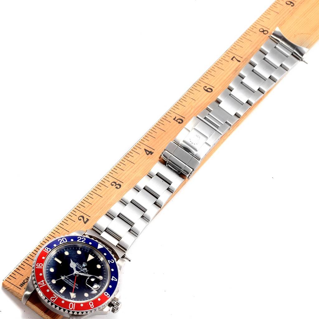 The Rolex GMT-Master 16710 Men's Stainless Steel Black Dial 16710 Men's Stainless Steel Black Dial watch is shown lying flat beside a ruler, displaying its face, bezel, and metal bracelet.
