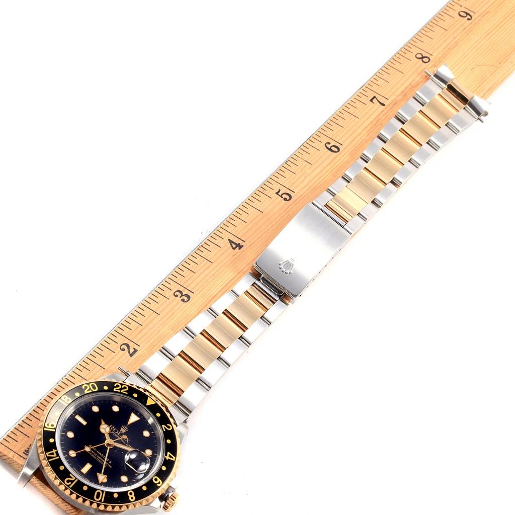 This image shows a side angle of a Rolex GMT-Master 16713 Men's Stainless Steel Black Dial 16713 Men's Stainless Steel Black Dial watch, featuring its dial, bezel, and two-tone bracelet alongside a measuring ruler.