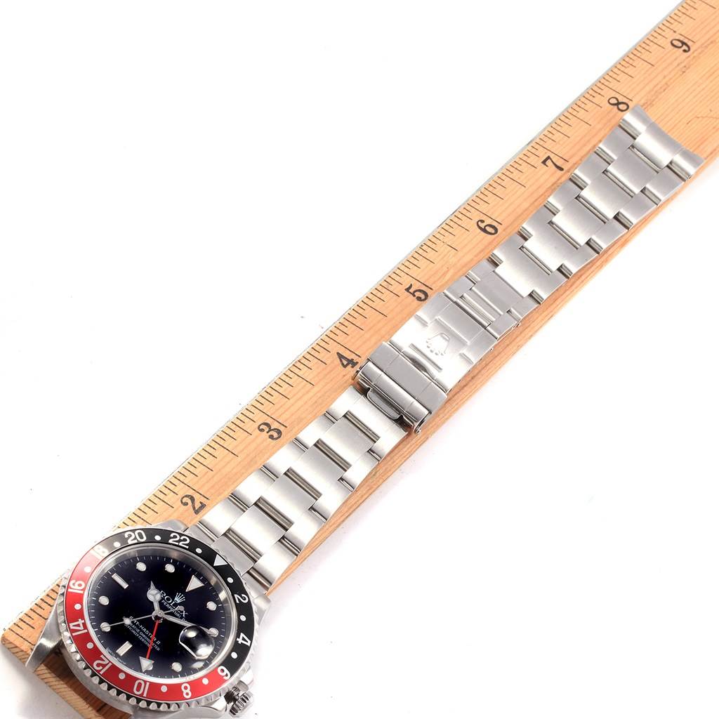The image shows a Rolex GMT-Master 16710 Men's Stainless Steel Black Dial 16710 Men's Stainless Steel Black Dial watch face and stainless steel bracelet lying flat beside a ruler.