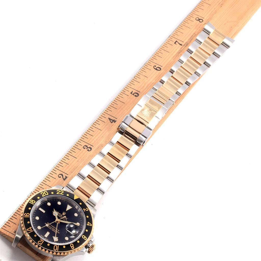 The image shows the full length of a Rolex GMT-Master 16713 Men
s Stainless Steel Black Dial 16713 Men
s Stainless Steel Black Dial watch, laid flat alongside a wooden ruler.