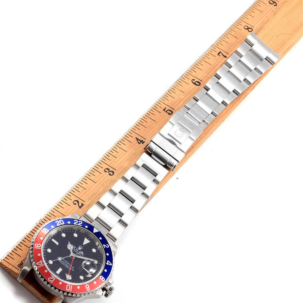 The Rolex GMT-Master 16710 Men's Stainless Steel Black Dial 16710 Men's Stainless Steel Black Dial watch is shown flat on a wooden ruler, displaying its face, bezel, bracelet, and clasp.