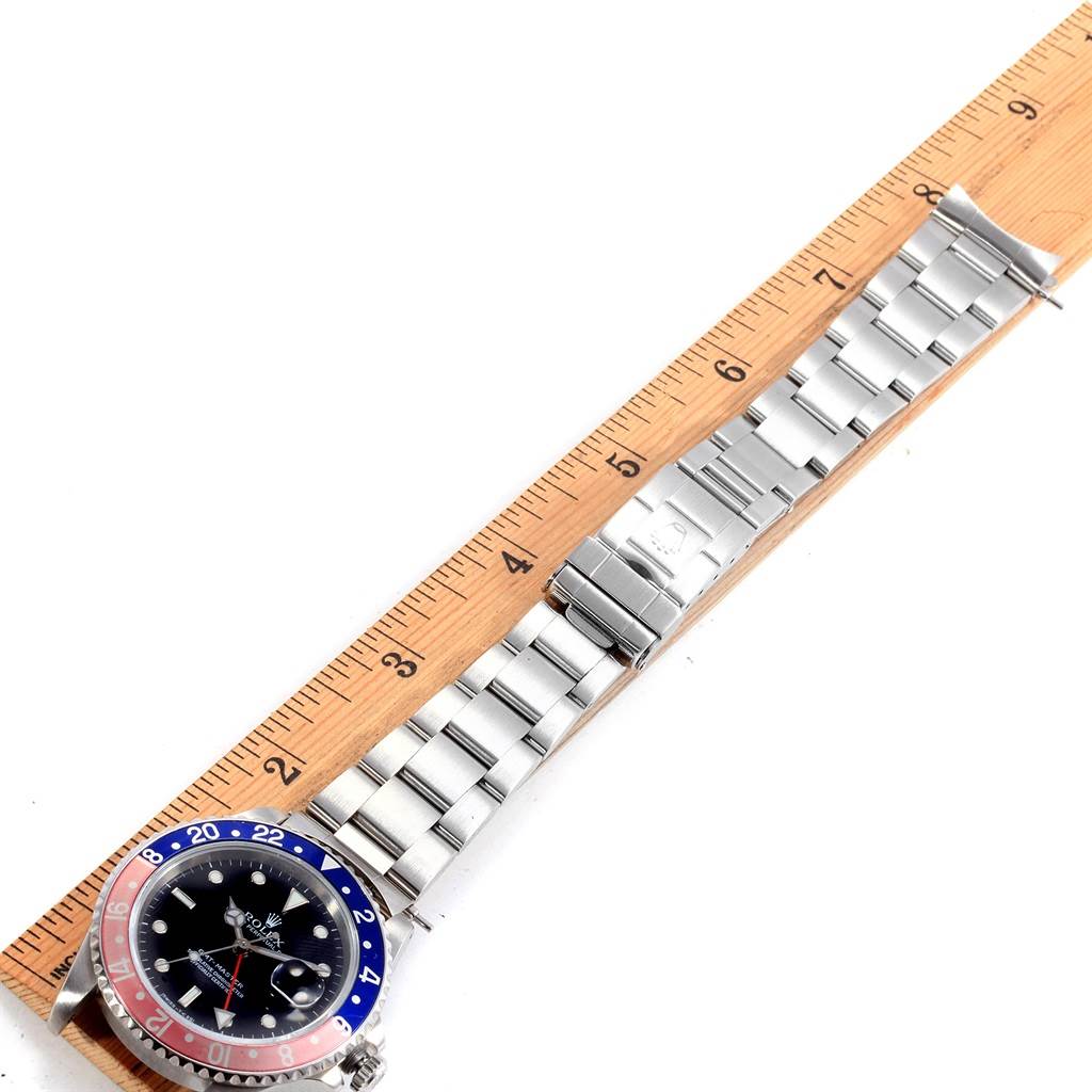 The image shows a top-down view of a Rolex GMT-Master 16700 Men's Stainless Steel Black Dial 16700 Men's Stainless Steel Black Dial watch, including its face and stainless steel bracelet, next to a ruler.