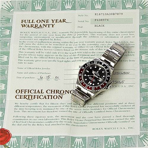 This image shows a Rolex GMT-Master 16710 Men's Stainless Steel Black Dial 16710 Men's Stainless Steel Black Dial watch placed on top of its warranty and official chronometer certification papers.
