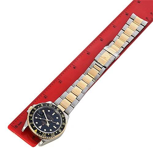 The image shows a Rolex GMT-Master 16713 Men's Stainless Steel Black Dial 16713 Men's Stainless Steel Black Dial watch laid flat on a red ruler, displaying its face, bezel, and two-tone bracelet.