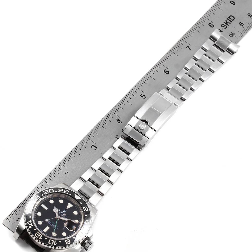 The Rolex GMT-Master 116710 Men's Stainless Steel Black Dial 116710 Men's Stainless Steel Black Dial watch is shown with its full strap extended, next to a ruler, displaying the face and clasp at an overhead angle.