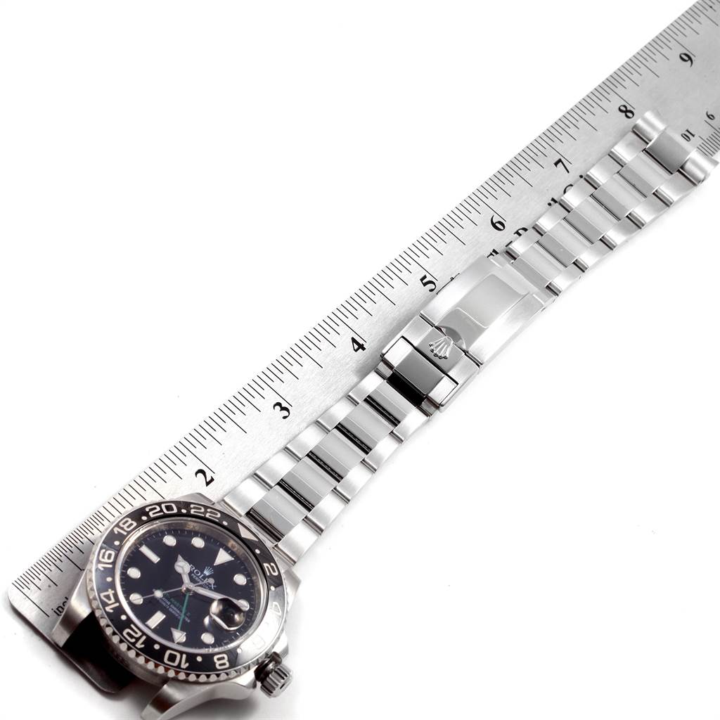 This image shows a Rolex GMT-Master 116710 Men's Stainless Steel Black Dial 116710 Men's Stainless Steel Black Dial watch face and bracelet lying parallel to a ruler.