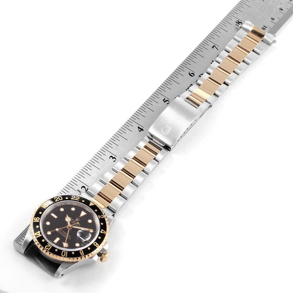 The Rolex GMT-Master 16713 Men's Stainless Steel Black Dial 16713 Men's Stainless Steel Black Dial watch is shown laid flat with the face and metal bracelet fully extended next to a ruler.