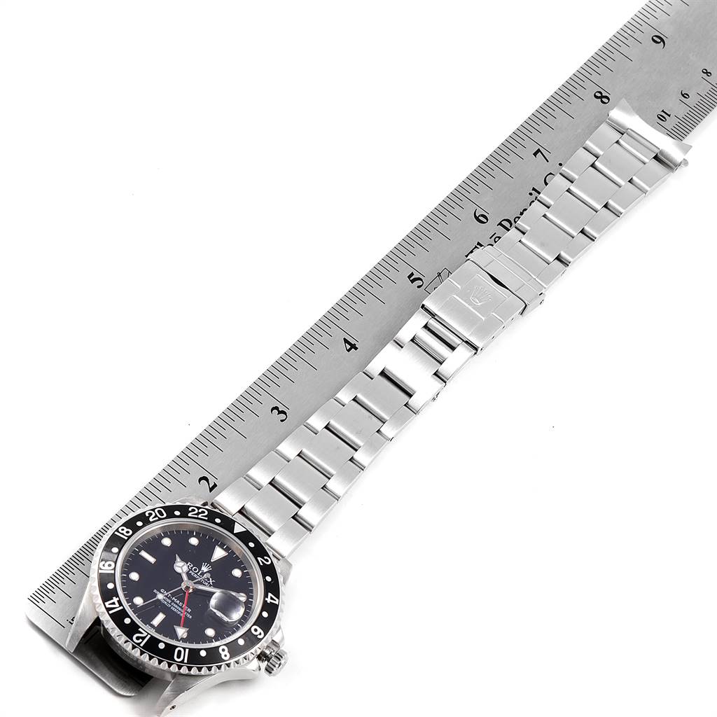 The image shows the Rolex GMT-Master 16700 Men's Stainless Steel Black Dial 16700 Men's Stainless Steel Black Dial watch face and its metal bracelet laid out along a ruler.