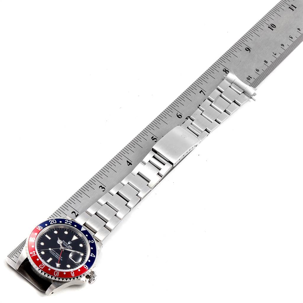 This image displays the Rolex GMT-Master 16700 Men's Stainless Steel Black Dial 16700 Men's Stainless Steel Black Dial watch from a top-down angle, showing the watch face, bezel, and extended bracelet alongside a measuring ruler.