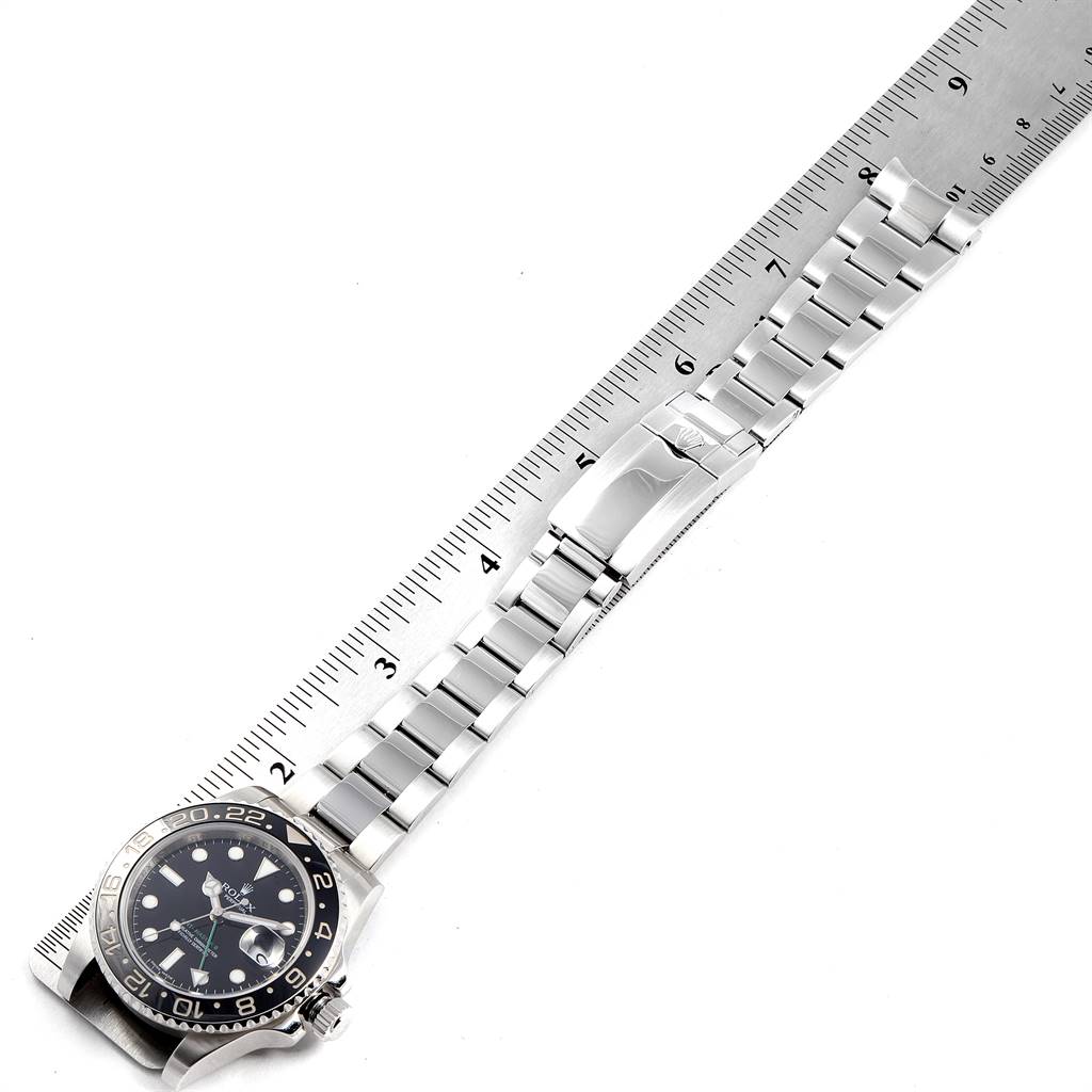 The image shows a top-down view of a Rolex GMT-Master 116710 Men's Stainless Steel Black Dial 116710 Men's Stainless Steel Black Dial watch and its metal bracelet alongside a ruler.