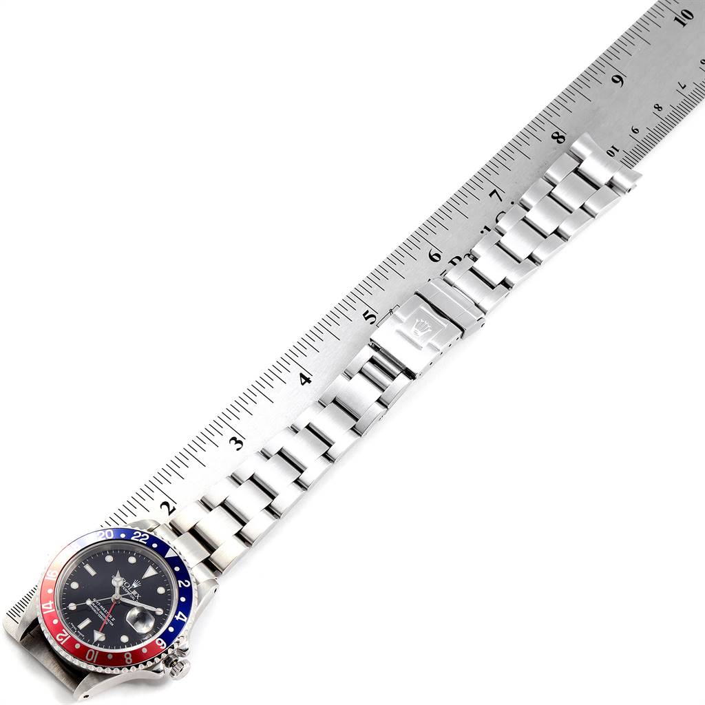 The Rolex GMT-Master 16710 Men's Stainless Steel Black Dial 16710 Men's Stainless Steel Black Dial watch is shown from an overhead angle, displaying its face, bezel, and bracelet with a measuring ruler alongside it.