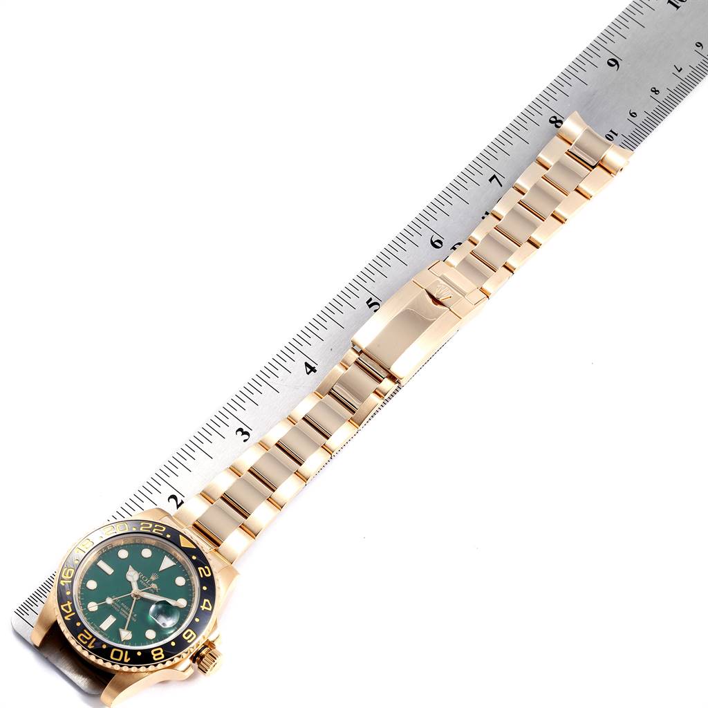 This image shows a top view of a Rolex GMT-Master 116718 Men's Yellow Gold Green Dial 116718 Men's Yellow Gold Green Dial watch with its full bracelet extended, alongside a ruler for scale.