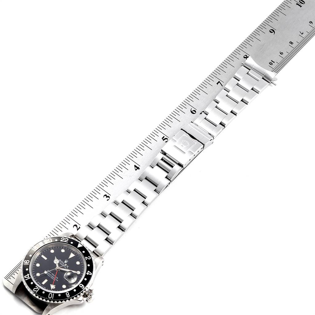 The image shows a Rolex GMT-Master 16700 Men's Stainless Steel Black Dial 16700 Men's Stainless Steel Black Dial watch laid flat next to a ruler, displaying its face and metal bracelet.