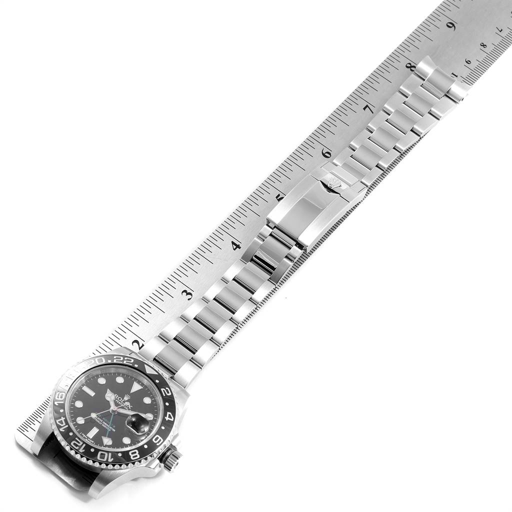 The image shows the front view of a Rolex GMT-Master 116710 Men's Stainless Steel Black Dial 116710 Men's Stainless Steel Black Dial watch including its face, bezel, bracelet, and clasp placed along a ruler.
