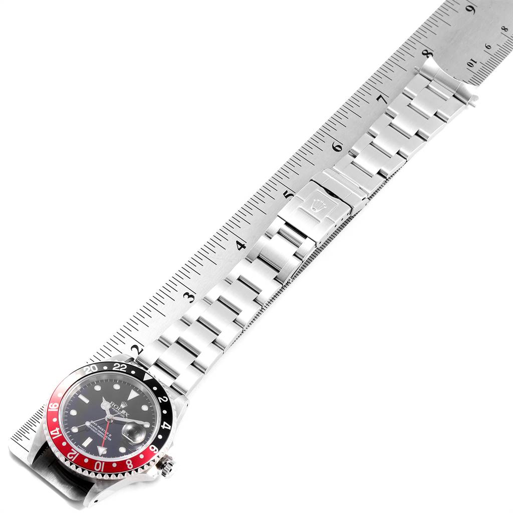 The image shows a top-down view of a Rolex GMT-Master 16710 Men
s Stainless Steel Black Dial 16710 Men
s Stainless Steel Black Dial watch, including the face, bezel, and stainless steel bracelet, placed on a ruler.