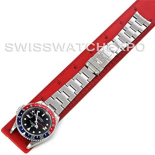 The image shows an overhead view of a Rolex GMT-Master 16710 Men's Stainless Steel Black Dial 16710 Men's Stainless Steel Black Dial watch, highlighting the face, bezel, and stainless steel bracelet placed on a red ruler.
